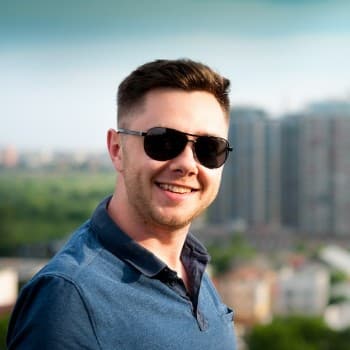 Smiling man in sunglasses and a blue polo shirt stands outdoors against a cityscape backdrop. Potential client for exterior cleaning services.