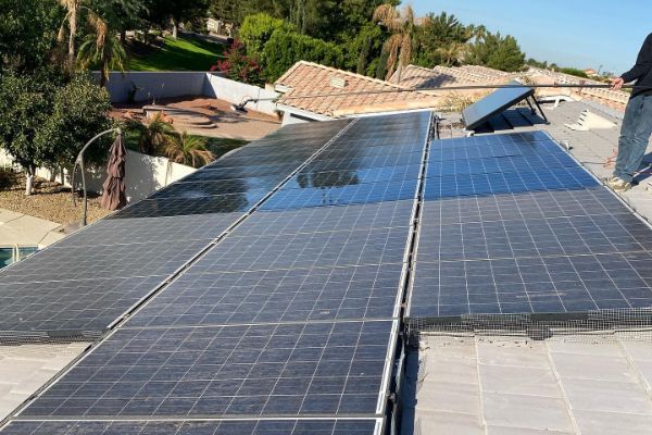 Solar panels on a home roof are being cleaned with a brush on a pole. This exterior cleaning helps maintain panel efficiency.