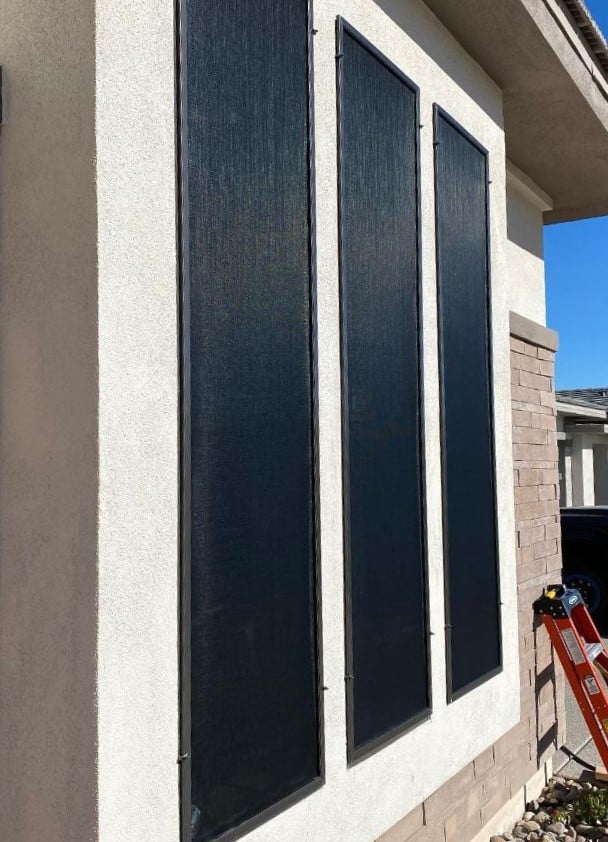 Three dark sun screens installed on a light stucco wall, part of a Sun Screen Installation in Gilbert AZ. The screens have dark frames and are vertically aligned.