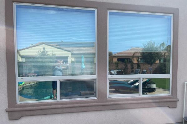 Windows reflecting a pool and backyard. The view through the glass shows a house, patio furniture, and a partially visible person, capturing an outdoor living scene.