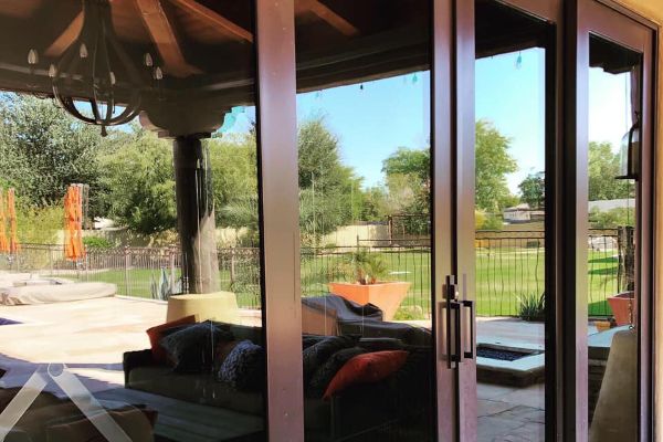 Patio view through sliding glass doors: outdoor seating, lush green lawn, and a glimpse of the surrounding neighborhood. The doors reflect the inviting outdoor space.