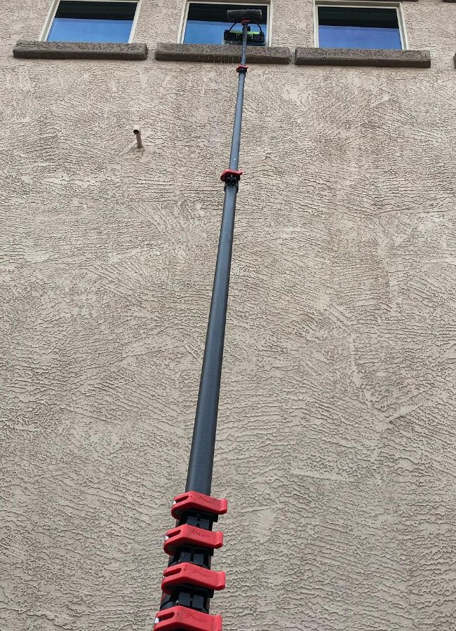 A telescopic pole with a squeegee reaches up to clean windows on a tan stucco house. This Gilbert AZ window cleaning setup allows for reaching high windows.